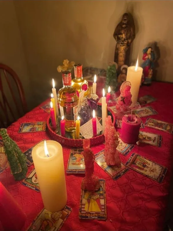 Mesa com toalha vermelha, velas acesas e cartas de tarô espalhadas ao redor.