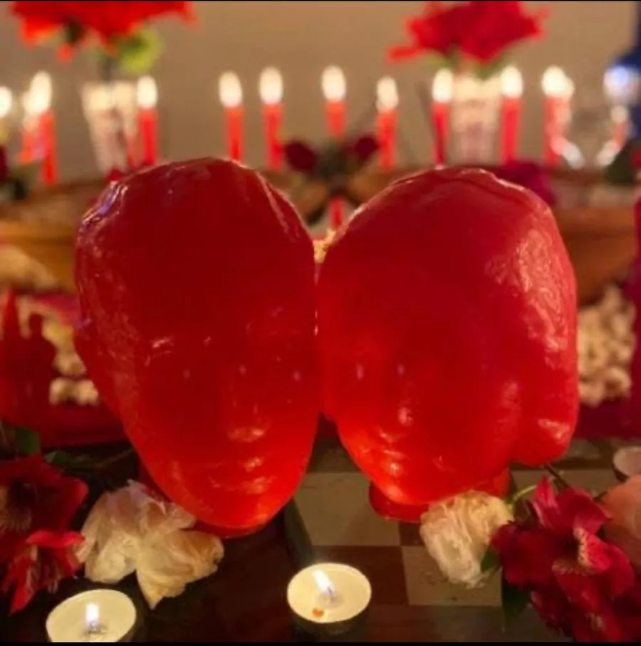 Duas velas vermelhas em forma de coração, entre flores vermelhas e muitas velas acesas.