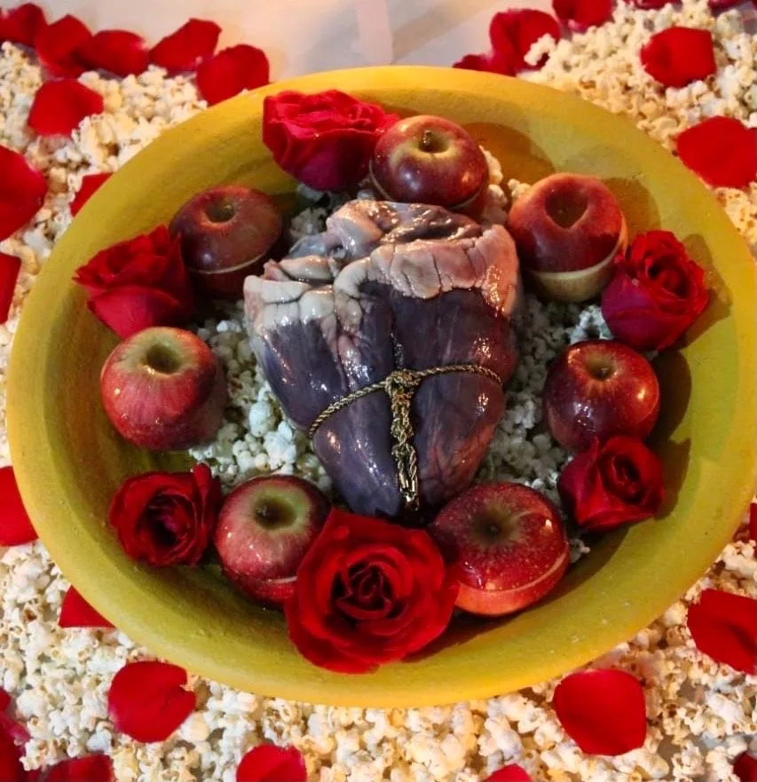 Prato com um coração envolto por maçãs, rosas vermelhas e pipoca, em uma oferenda.
